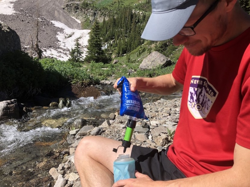 sawyer mini - eddy filters water into his hand bottle during a long run. he takes...