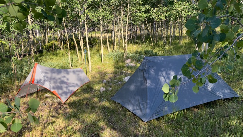 ultralight tent - a shaped tarp tent next to a double-walled trekking pole tent shows...